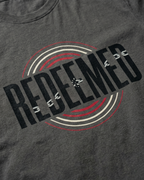 Detail shot of Christian Streetwear “Redeemed” graphic t-shirt in Asphalt Gray, featuring bold typography with broken chain symbolism and circular red and white accent design.