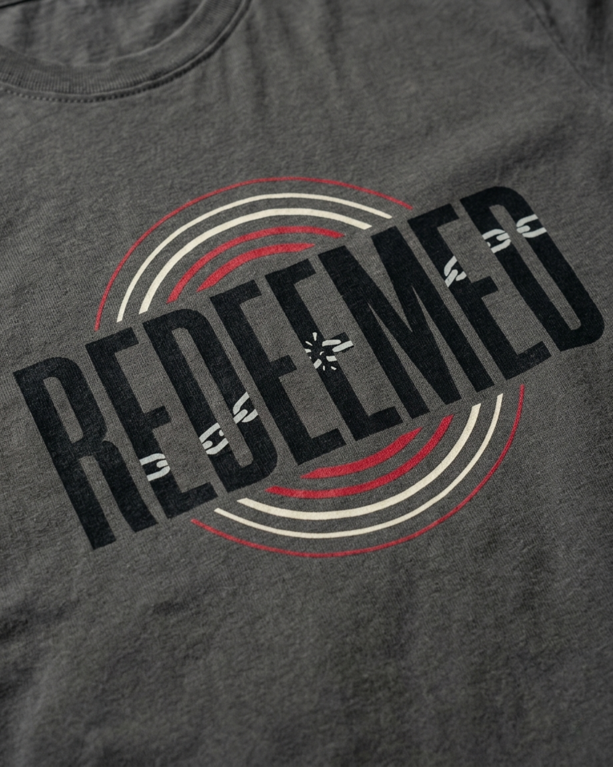 Detail shot of Christian Streetwear “Redeemed” graphic t-shirt in Asphalt Gray, featuring bold typography with broken chain symbolism and circular red and white accent design.