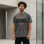 A man wearing a Christian Streetwear apparel “Redeemed” graphic t-shirt in Asphalt Gray, featuring bold typography with broken chain symbolism and circular red and white accent design.